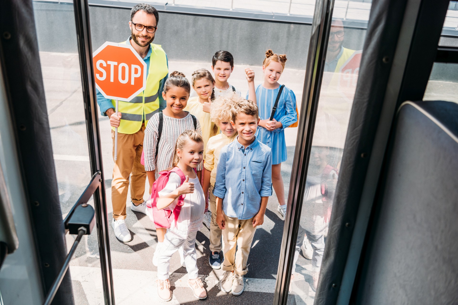 view from school bus at group of happy scholars with traffic guard looking at camera